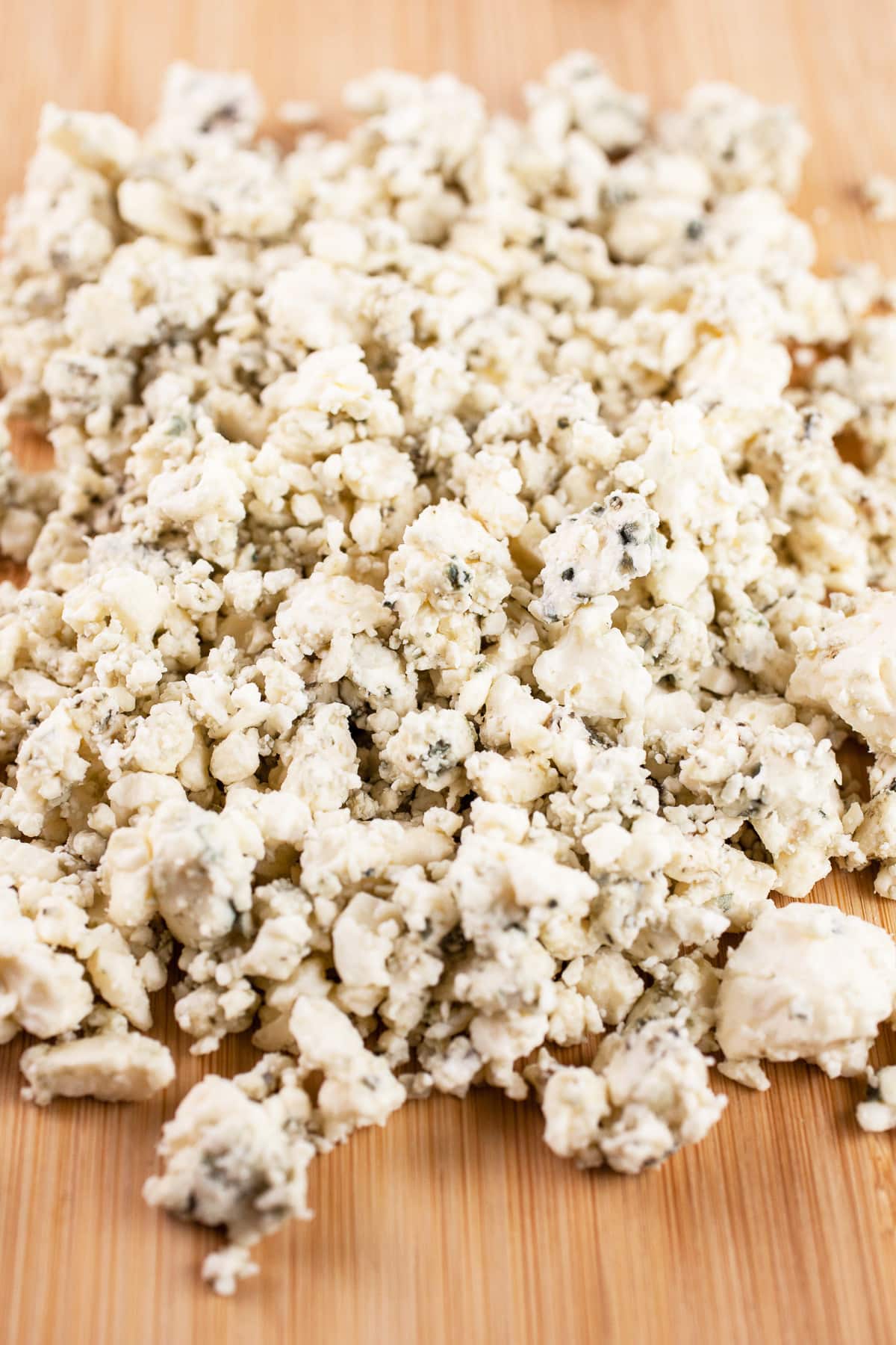 Blue cheese crumbles on wooden cutting board.