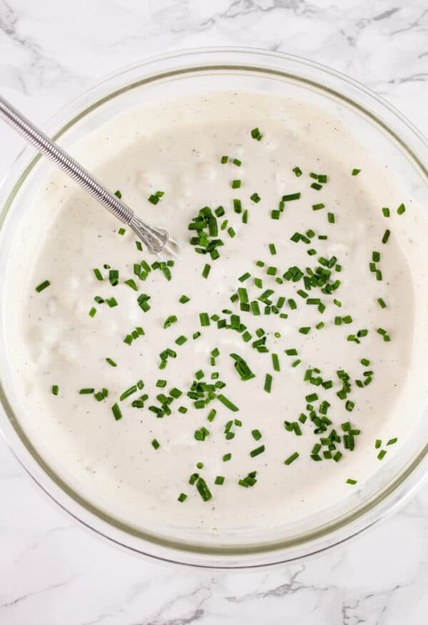 Blue cheese dressing with minced fresh chives in glass bowl with small whisk.