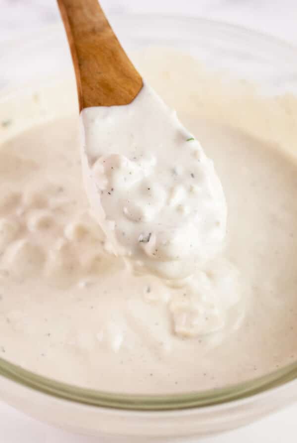 Wooden spoonful of blue cheese dressing lifted from glass bowl.