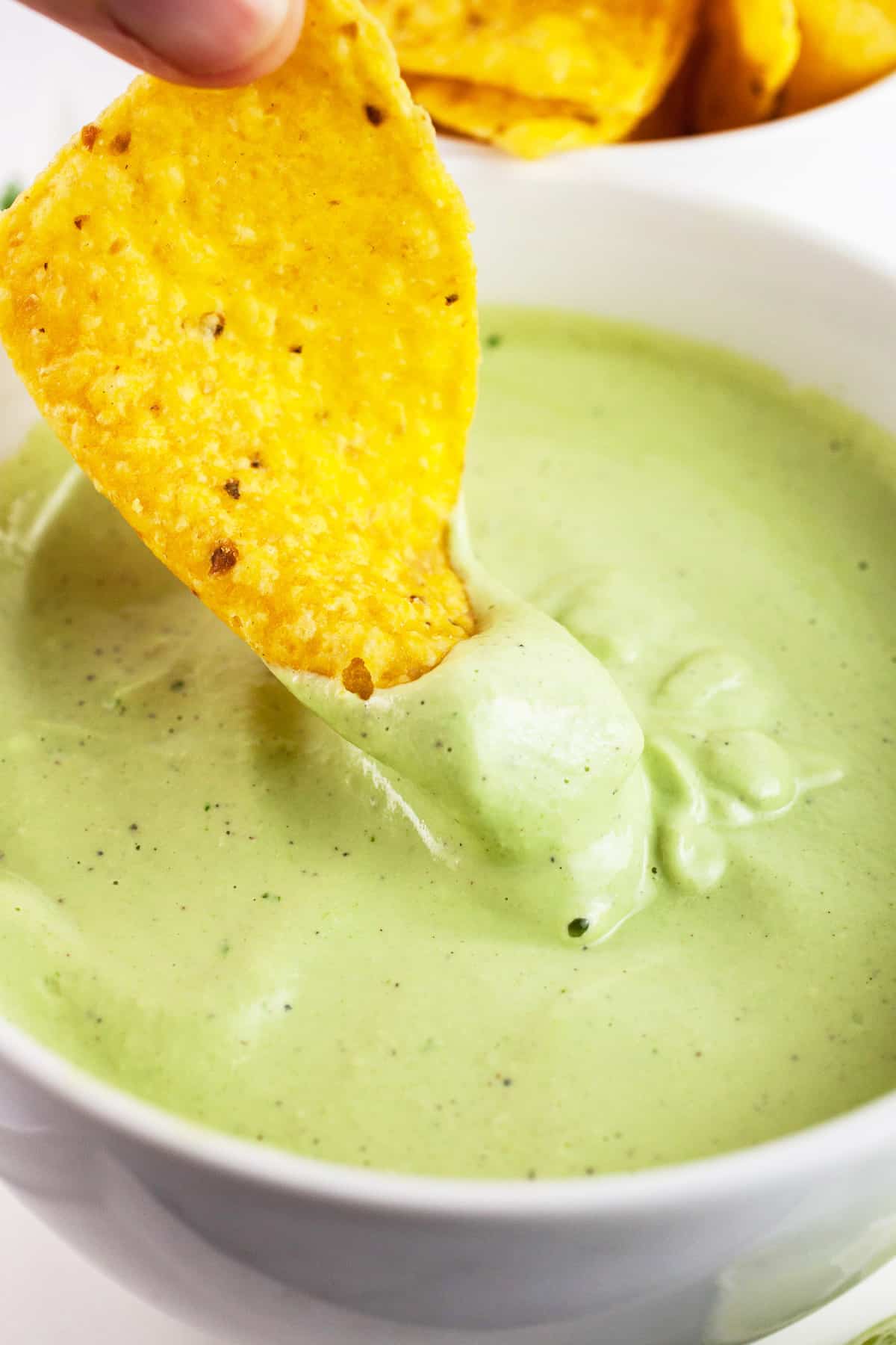 Tortilla chip dipped into white bowl of cashew cilantro sauce.