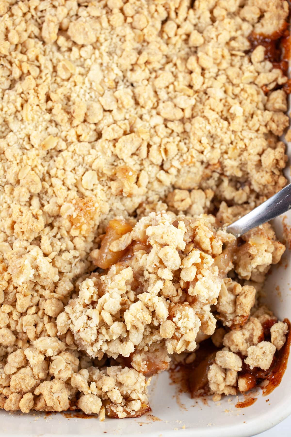 Metal spoon placed in baked apple crisp in ceramic baking dish.