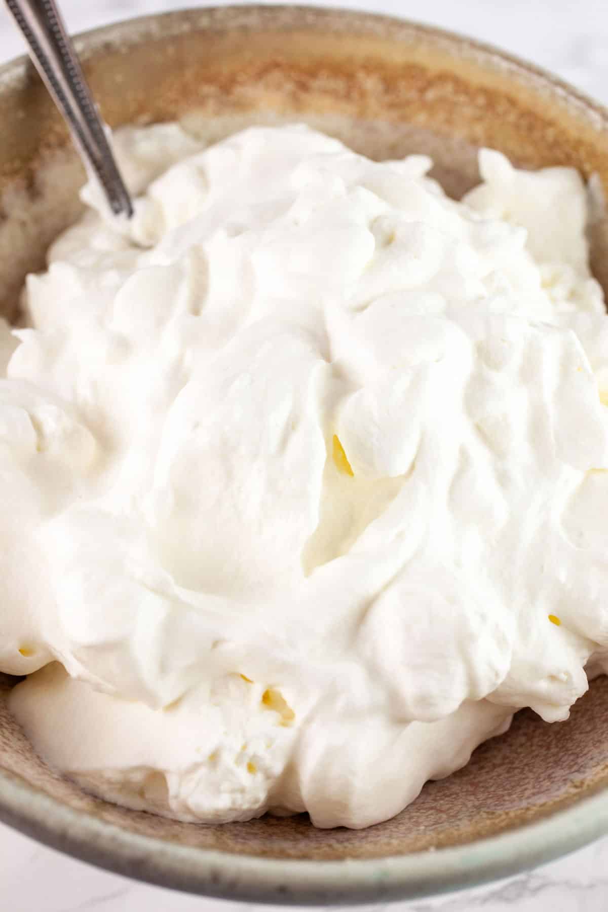 Homemade whipped cream in ceramic bowl with spoon.