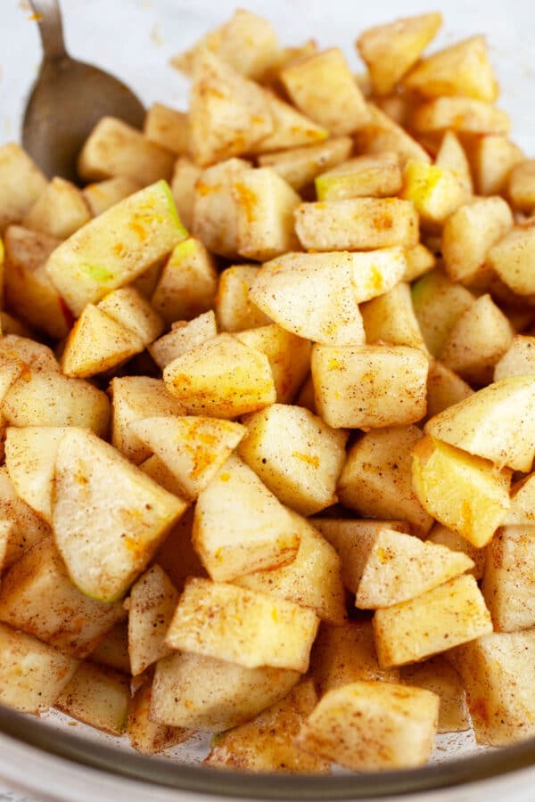 Raw diced apples tossed with sugar and spices in large glass mixing bowl.