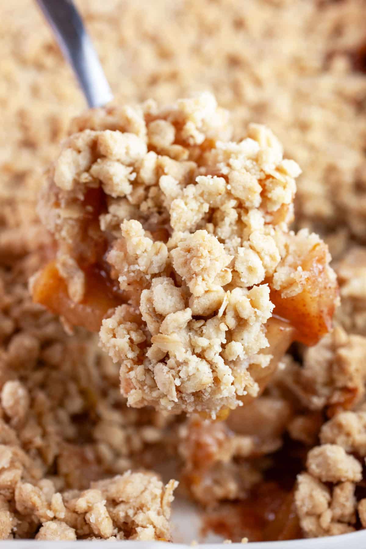 Scoop of apple crisp lifted from baking dish with metal spoon.