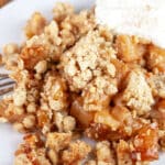 Gluten free apple crisp with whipped cream on white plate with fork.