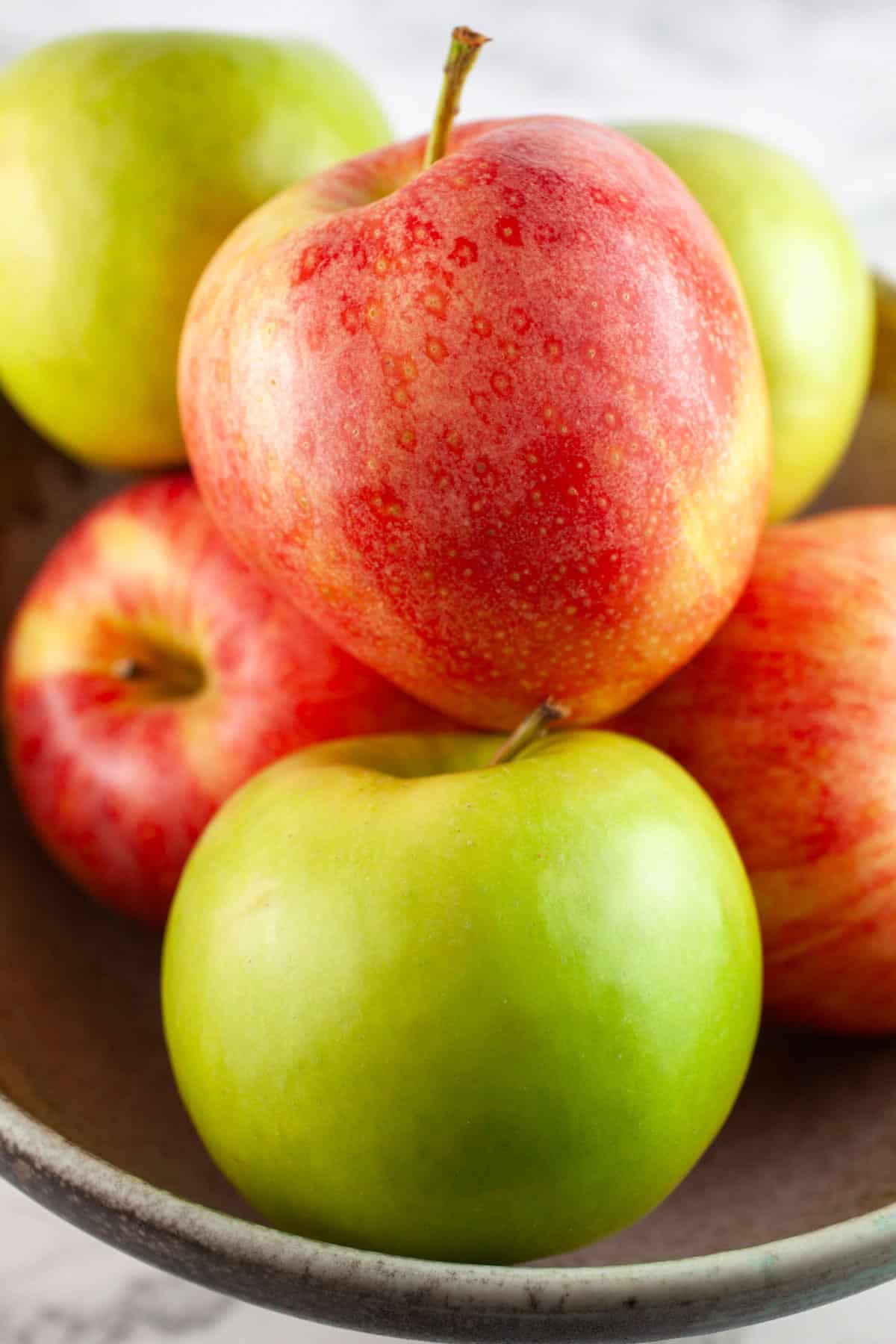 Whole Gala and Granny Smith apples in ceramic dish.