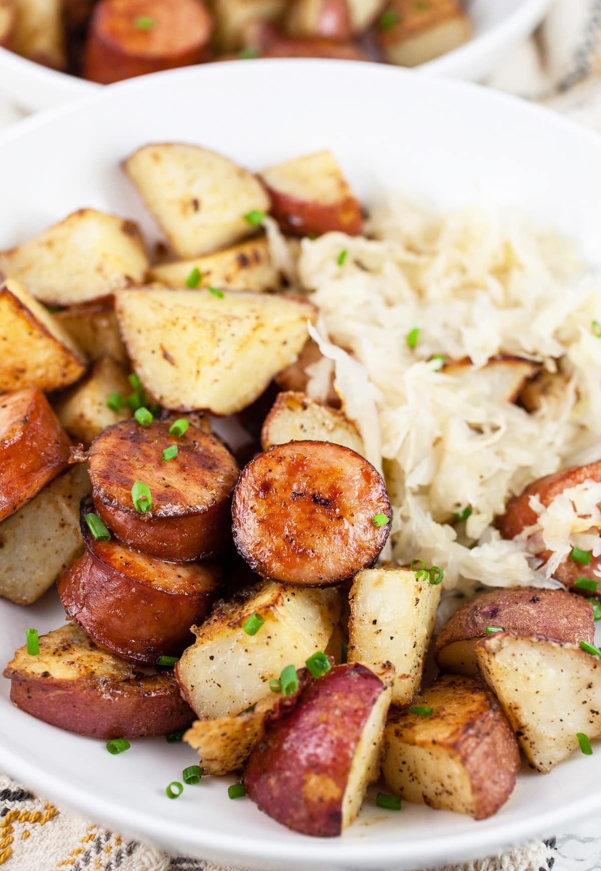 Sheet pan sausage and potatoes with sauerkraut in white bowls.