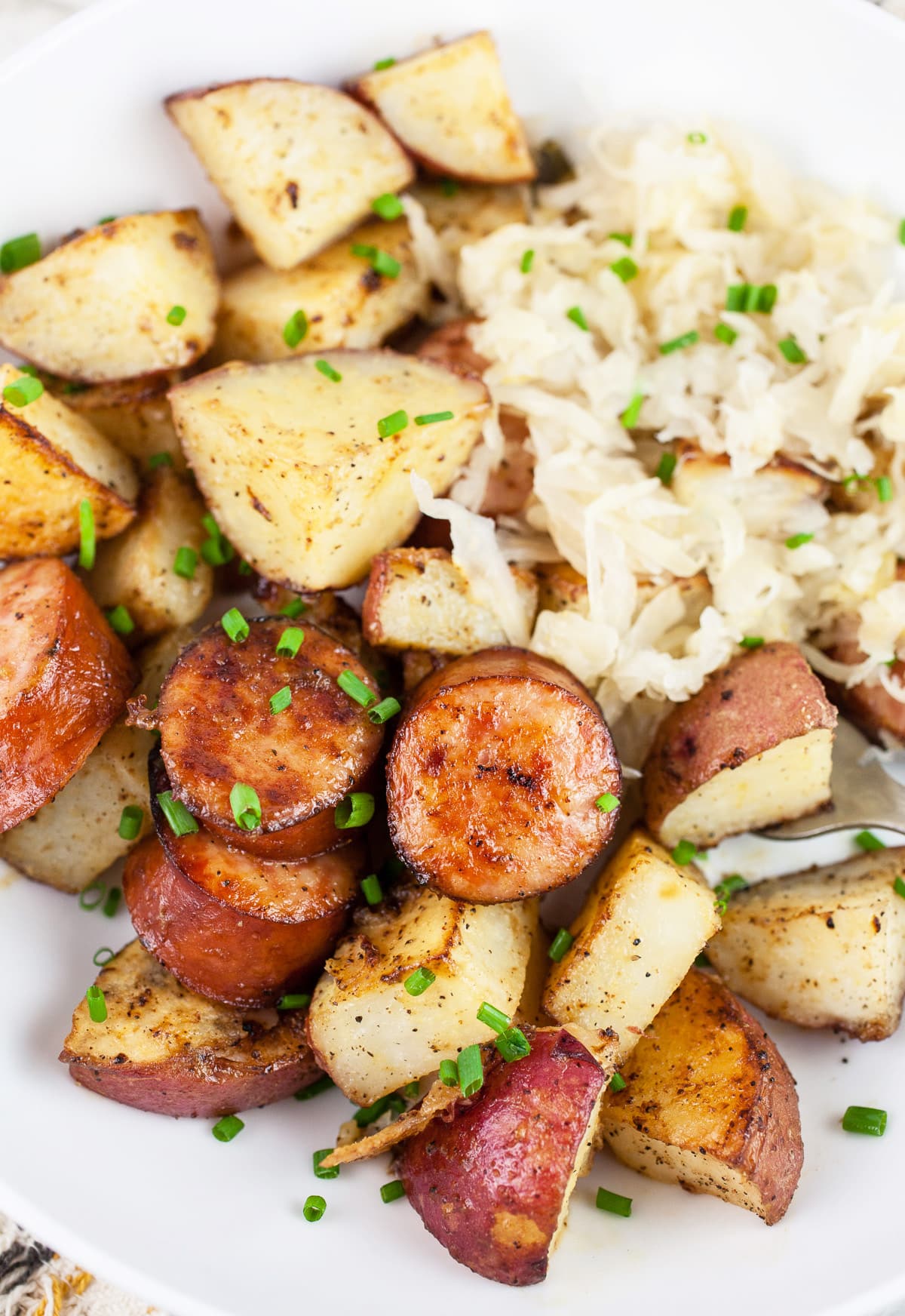 Sheet pan sausage and potatoes with sauerkraut in white bowl garnished with minced chives.