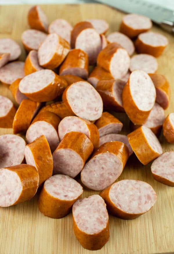 Sliced smoked sausages on wooden cutting board.