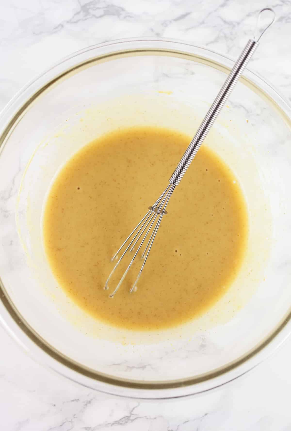 Maple mustard sauce in glass bowl with small whisk.