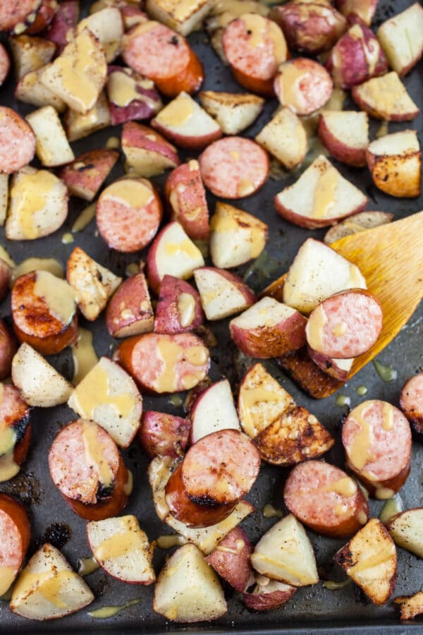 Roasted sausage and potatoes with maple mustard glaze on baking sheet.