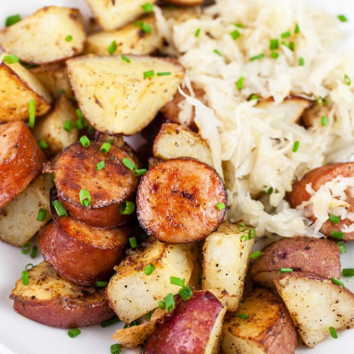 Sheet pan sausage and potatoes with sauerkraut in white bowl.