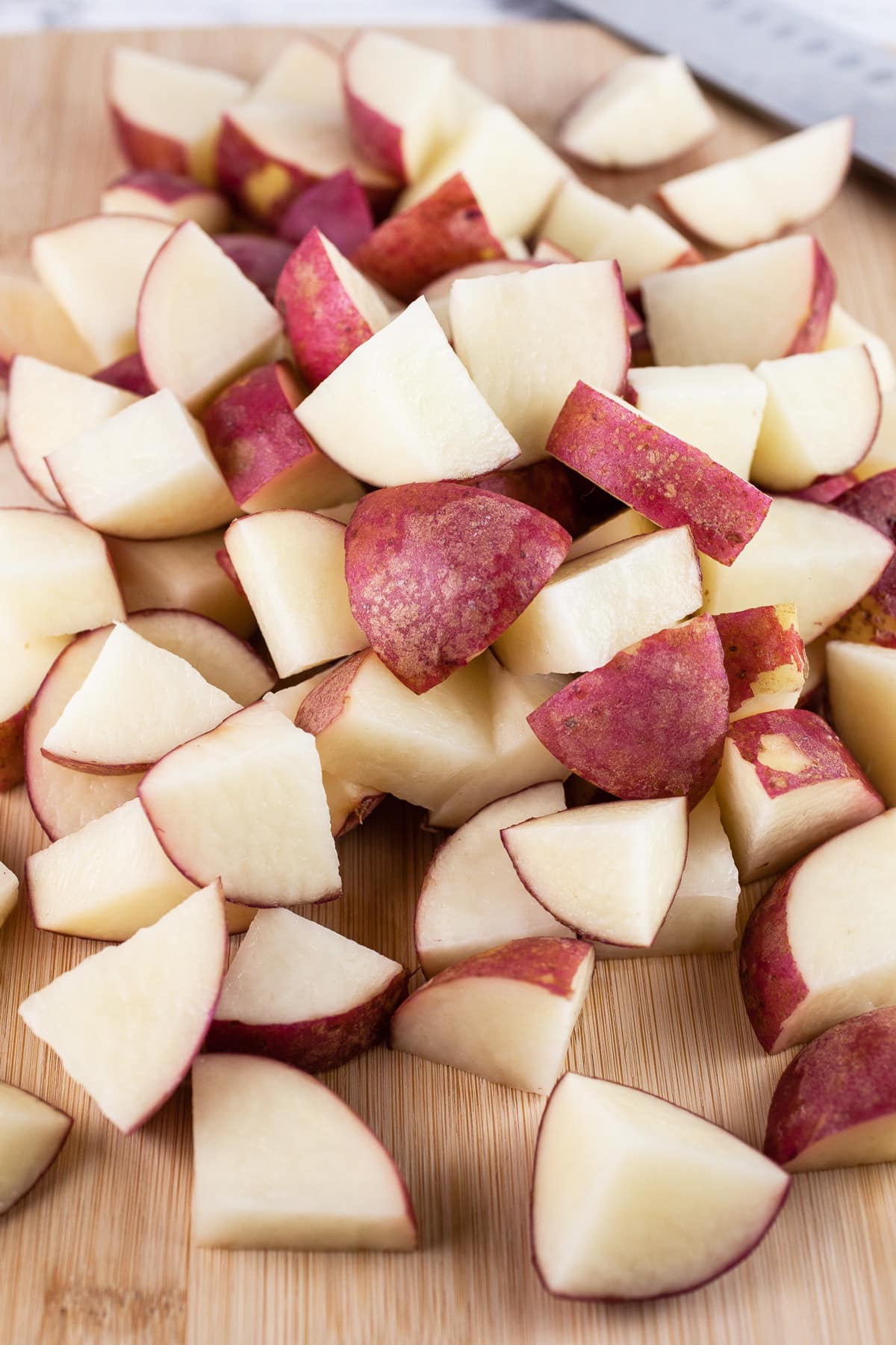 Diced red potatoes on wooden cutting board with knife.