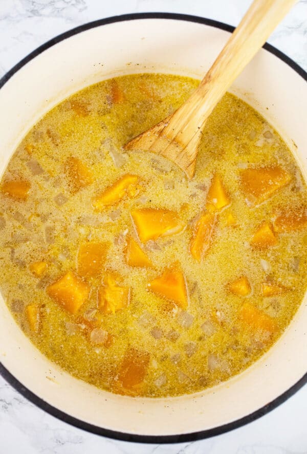 Cooked butternut squash soup in Dutch oven with wooden spoon.