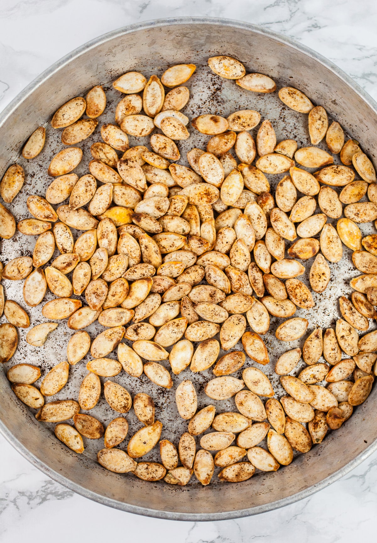Pumpkin seeds roasted with smoked paprika in round metal pan.
