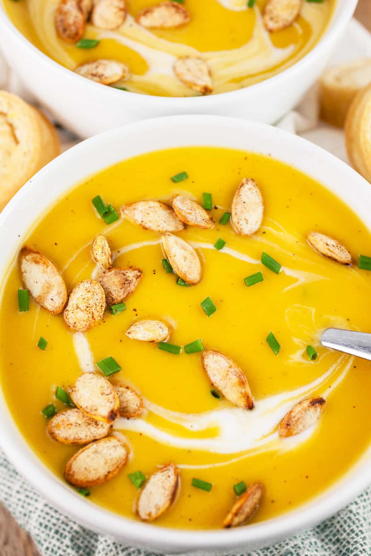 This Creamy Vegan Butternut Squash Soup is healthy, vegan, and super easy to make! In fact, it's one of the easiest soup recipes I've ever made. This soup is made with coconut milk and topped with roasted spicy pepitas. It's savory, sweet, and spicy at the same time. The perfect soup for fall or anytime! #butternutsquash #soup #vegan #coconutmilk Butternut squash soup with pumpkin seeds and minced chives in white bowls with spoons.