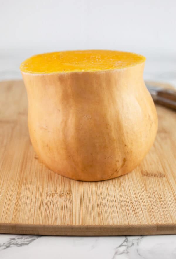 Butternut squash cut in half on wooden cutting board with knife.