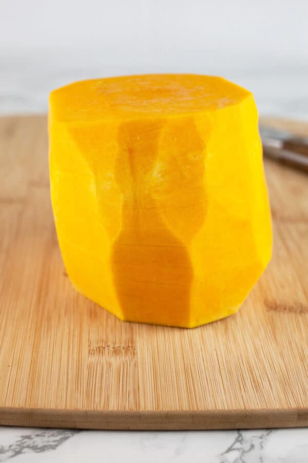 Butternut squash peeled and cut in half on wooden cutting board with knife.