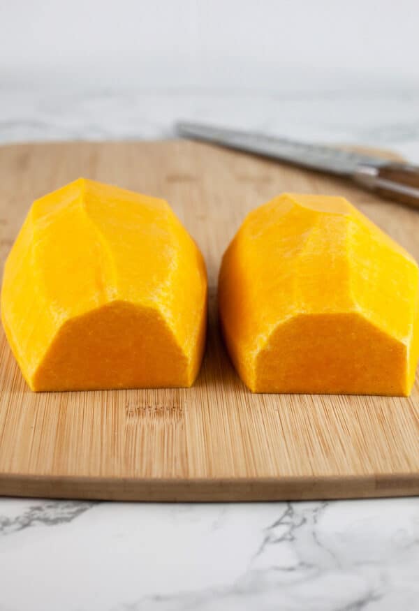 Peeled butternut squash half cut into halves on wooden cutting board with knife.