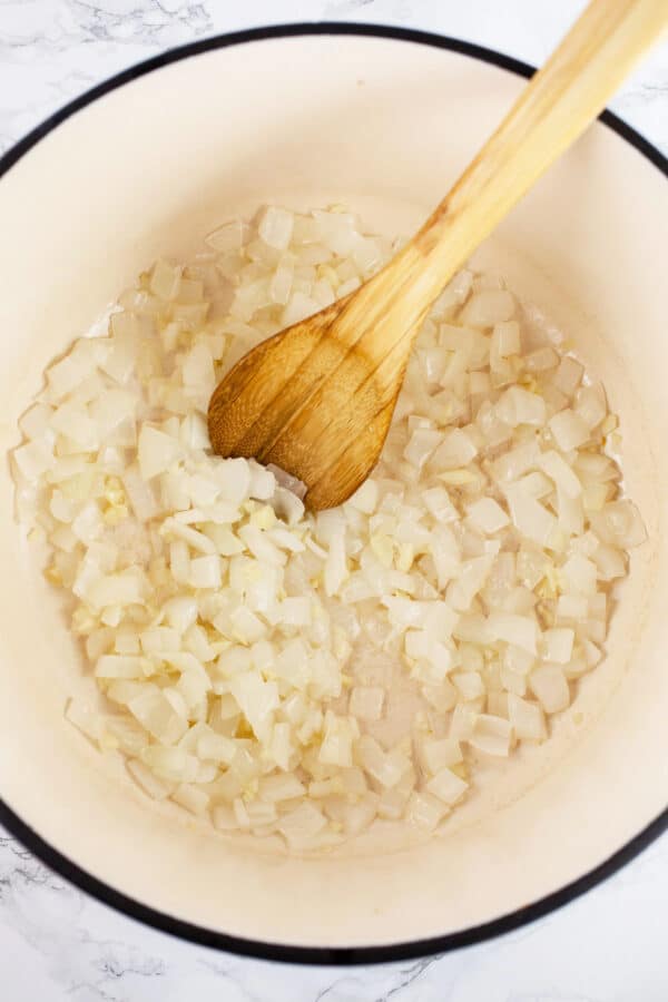 Minced garlic and onions sautéed in Dutch oven with wooden spoon.