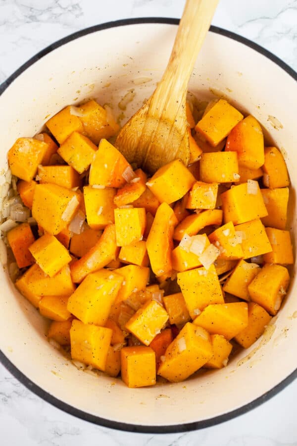 Garlic, onions, and cubed butternut squash sautéed in Dutch oven with wooden spoon.