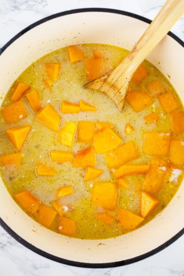 Uncooked butternut squash soup in Dutch oven with wooden spoon.