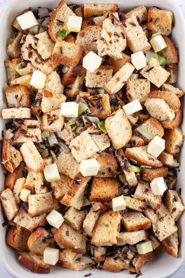 Uncooked stuffing dotted with butter in casserole dish.