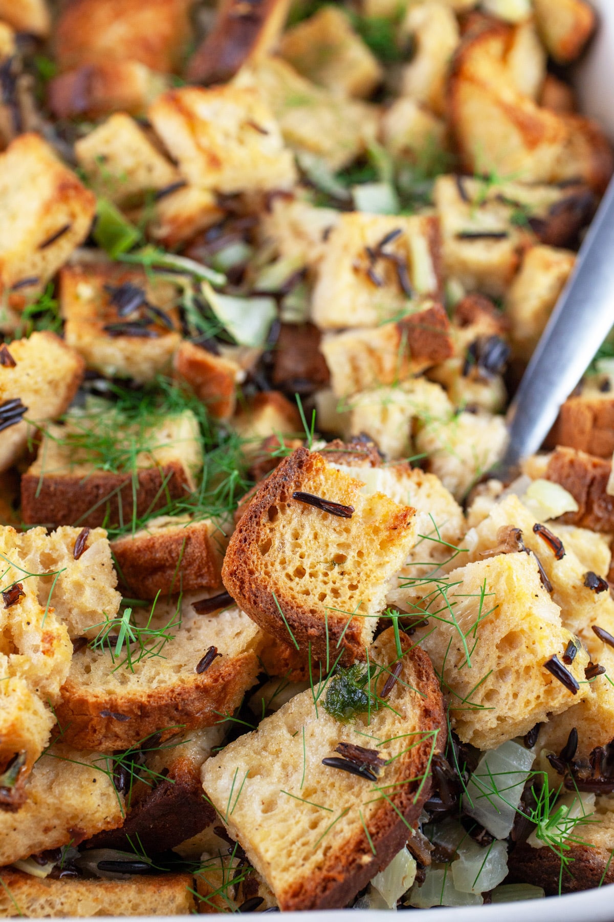 Cooked fennel wild rice stuffing in casserole dish with metal spoon.
