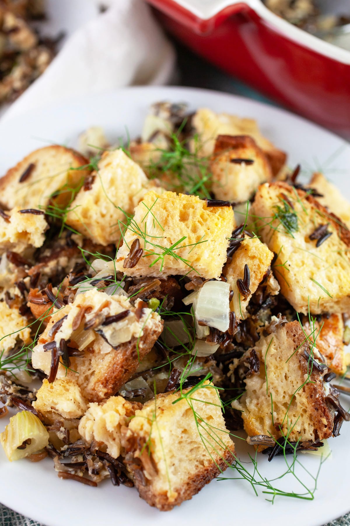 Wild rice fennel stuffing on white plate next to red casserole dish.