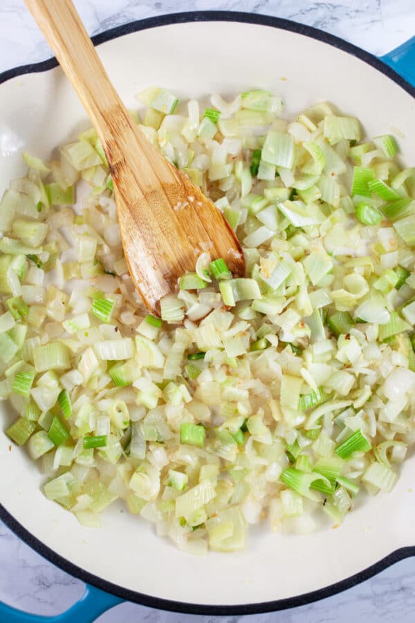 Minced garlic, onions, and fennel sauteed in a skillet with wooden spoon.