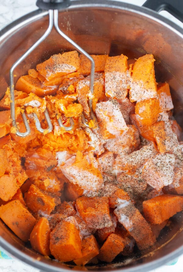 Cooked diced sweet potatoes with buttermilk and spices in pot with potato masher.