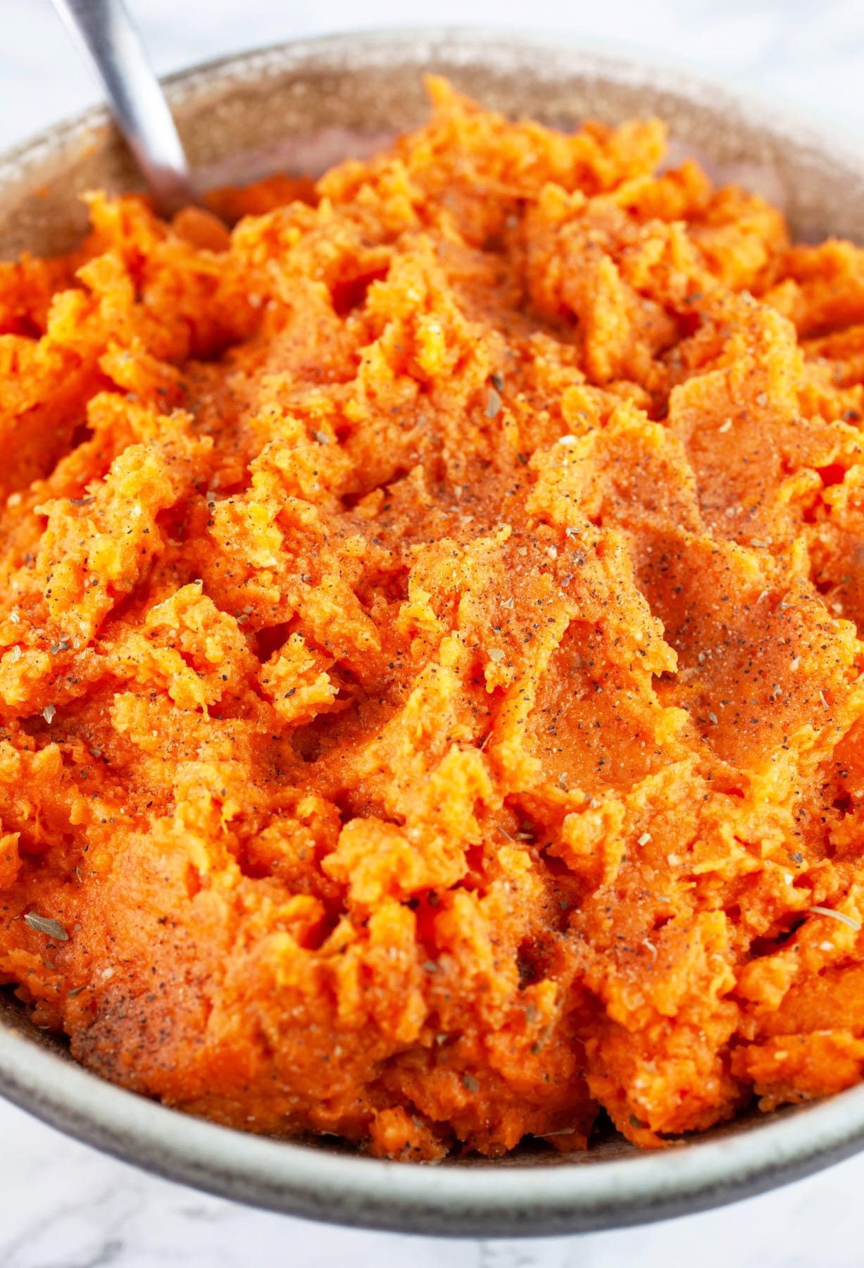 Mashed sweet potatoes in ceramic bowl with spoon.