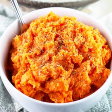 Savory mashed sweet potatoes in white bowl with fork.