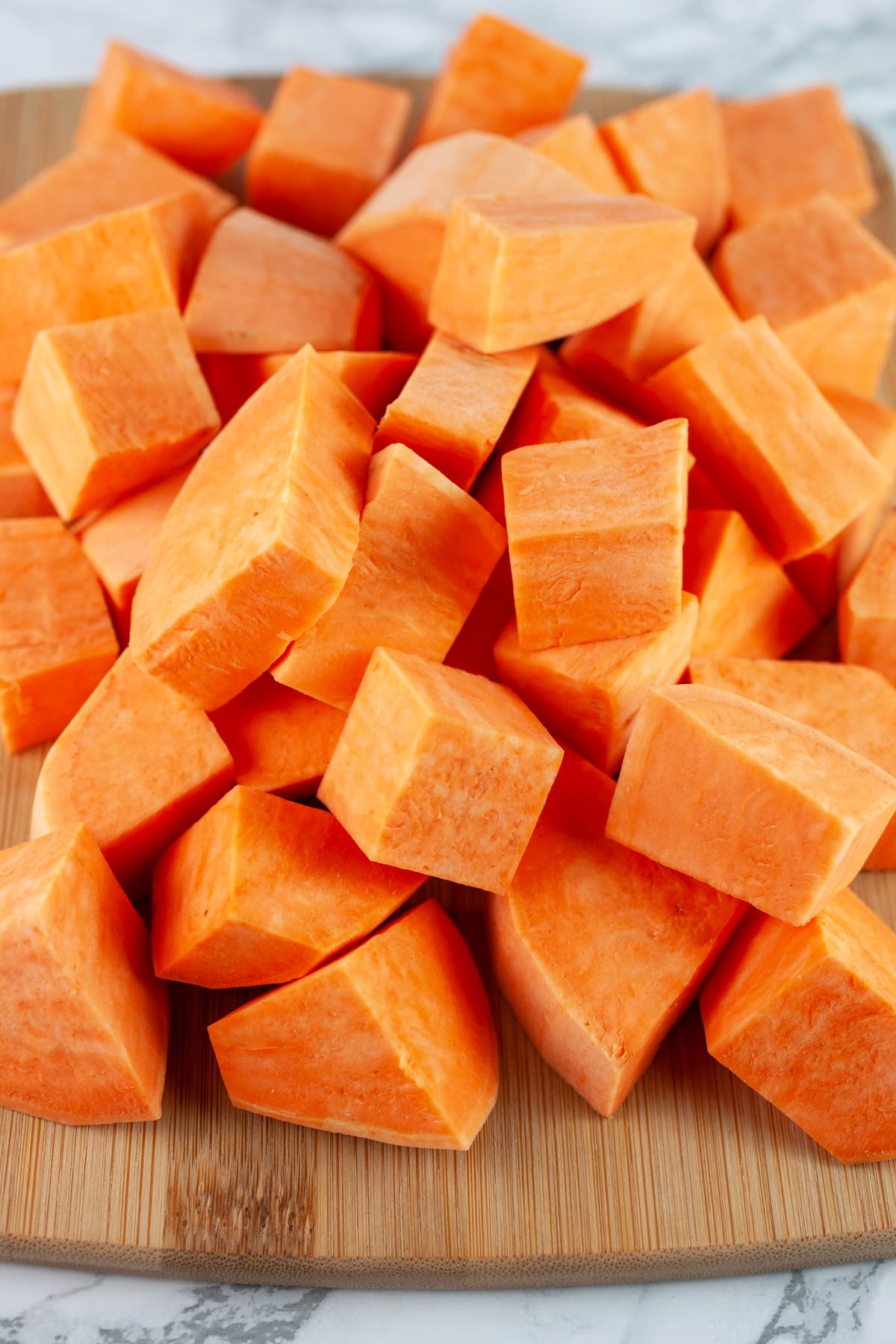 Peeled and diced sweet potatoes on wooden cutting board.