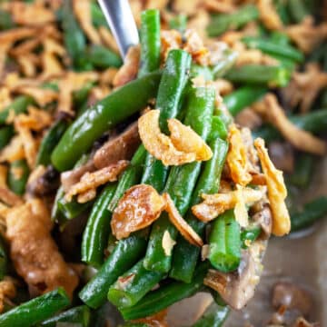 Scoop of green bean casserole lifted from casserole dish with metal spoon.
