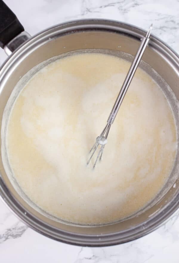 Butter, flour, and milk mixture in sauce pan with small whisk.