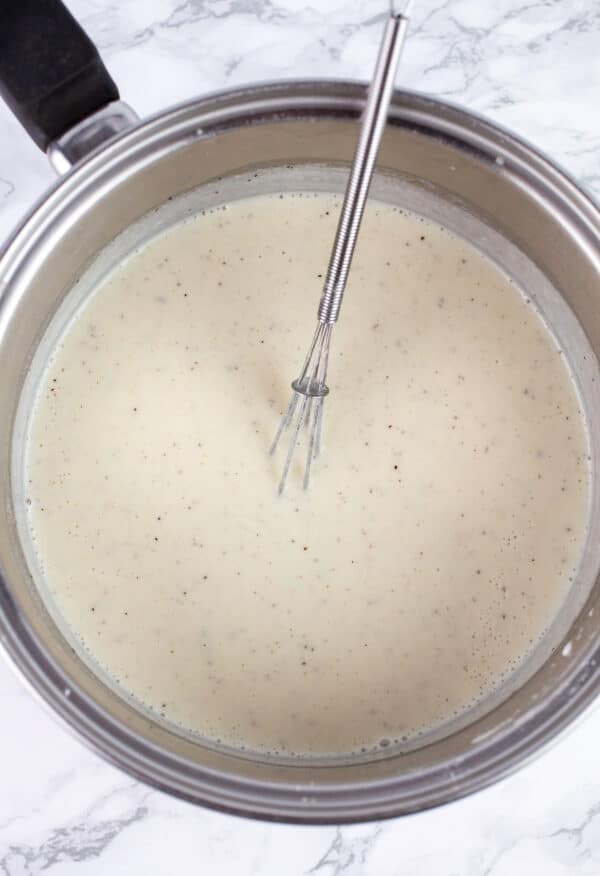 Thickened creamy mixture in sauce pan with small whisk.
