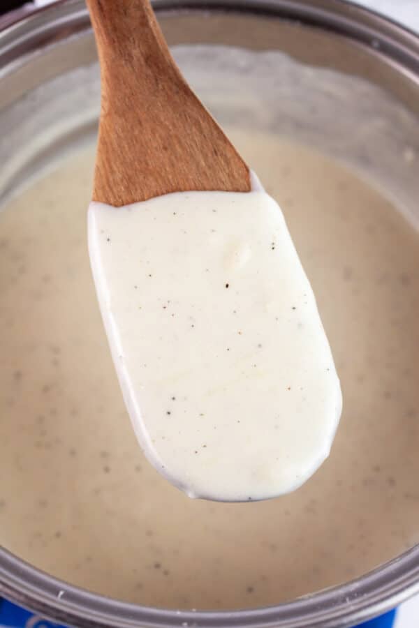 Cheese sauce lifted from sauce pan with wooden spoon.