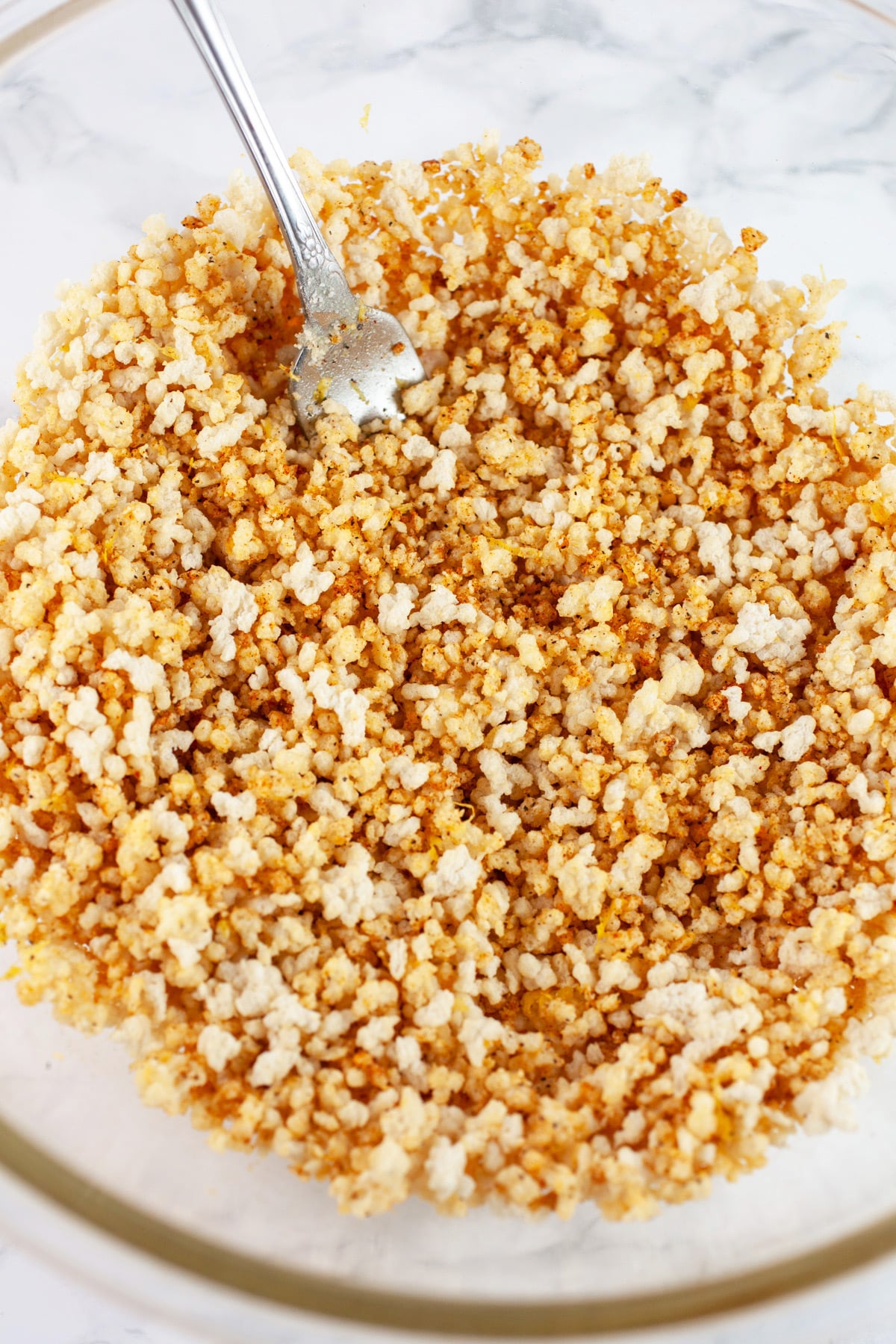 Spiced breadcrumb mixture in large glass bowl with fork.