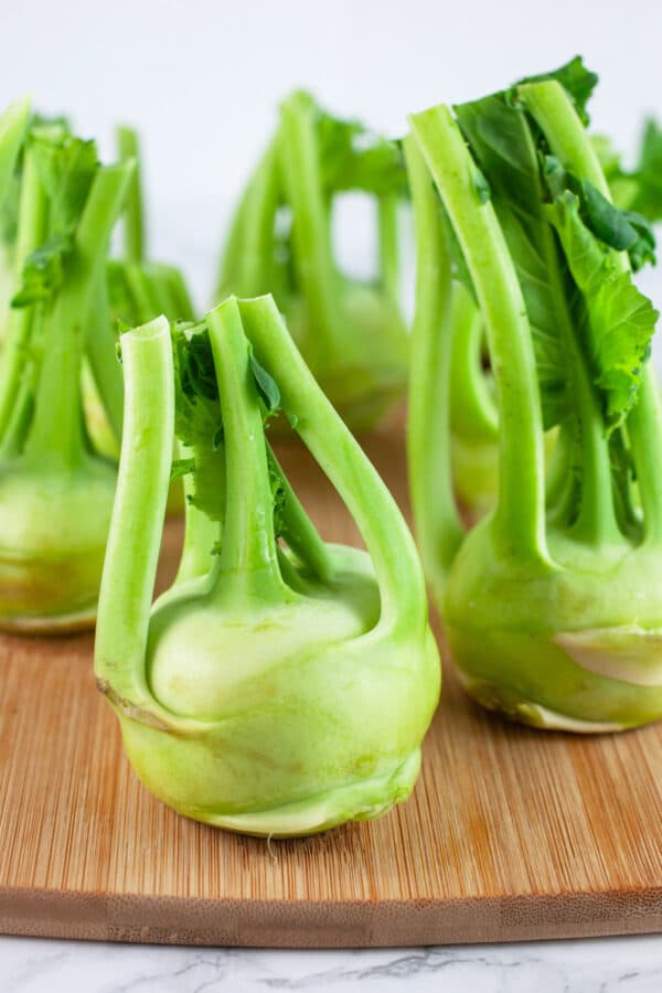 Kohlrabi with bottoms cut off standing on wooden cutting board.