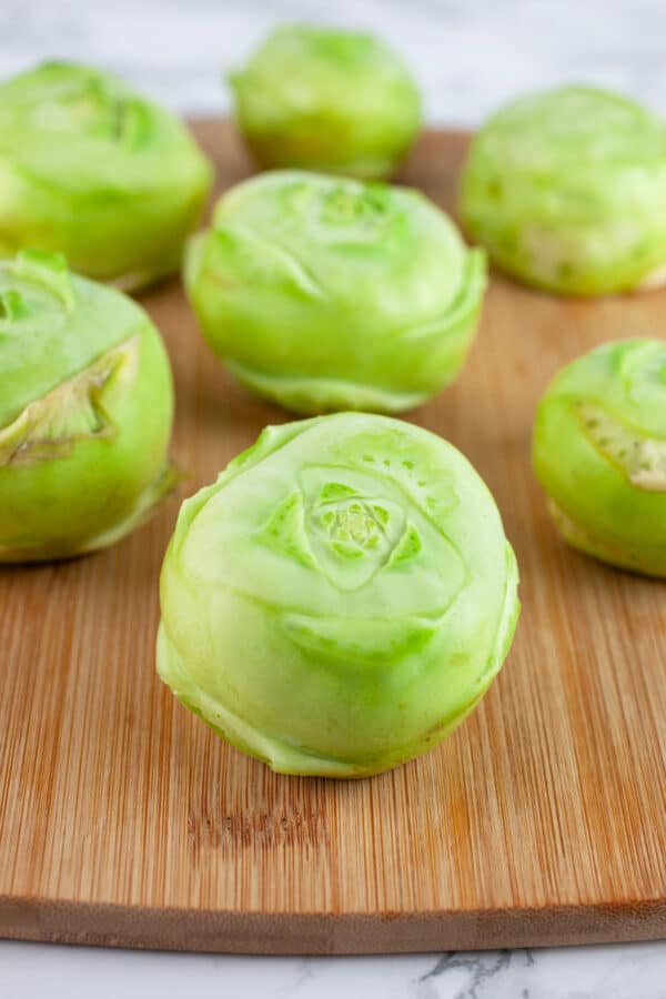 Unpeeled kohlrabi with stems and leaves trimmed on wooden cutting board.