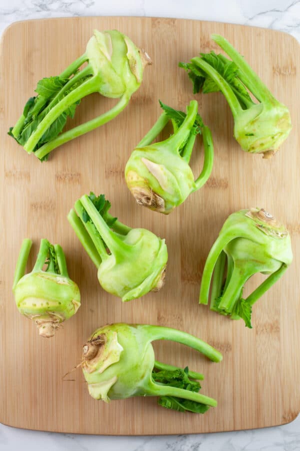 Whole kohlrabi scattered on wooden cutting board.