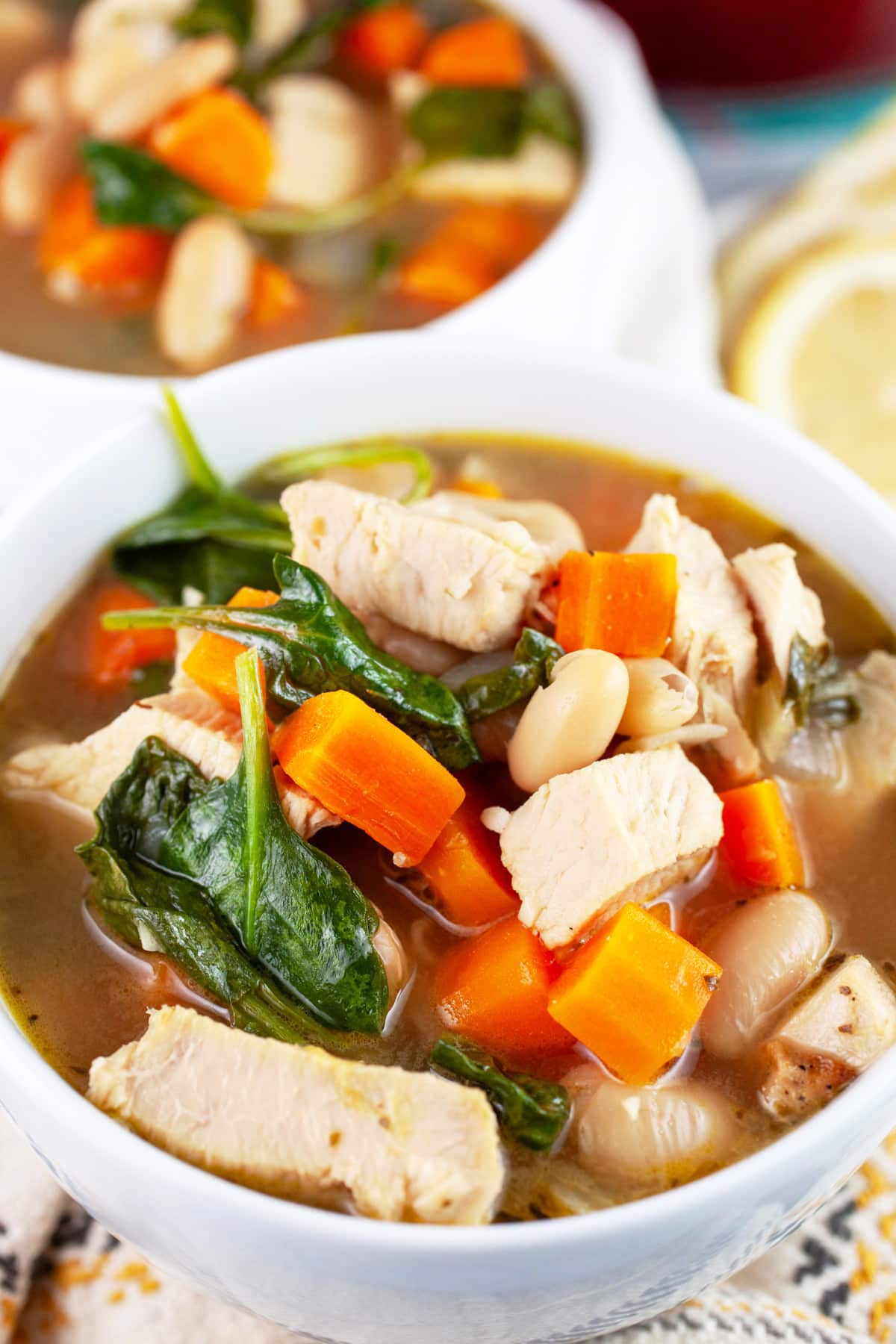 Turkey white bean soup with carrots and spinach in white bowls next to lemon wheels.