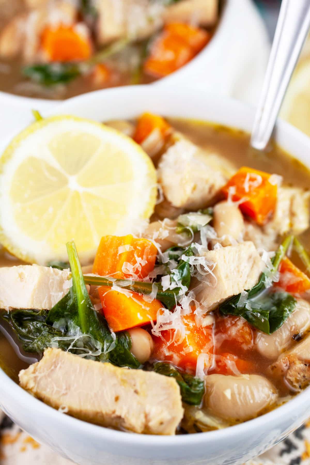 White bean turkey soup with Parmesan cheese and lemon wheel in white bowl with spoon.