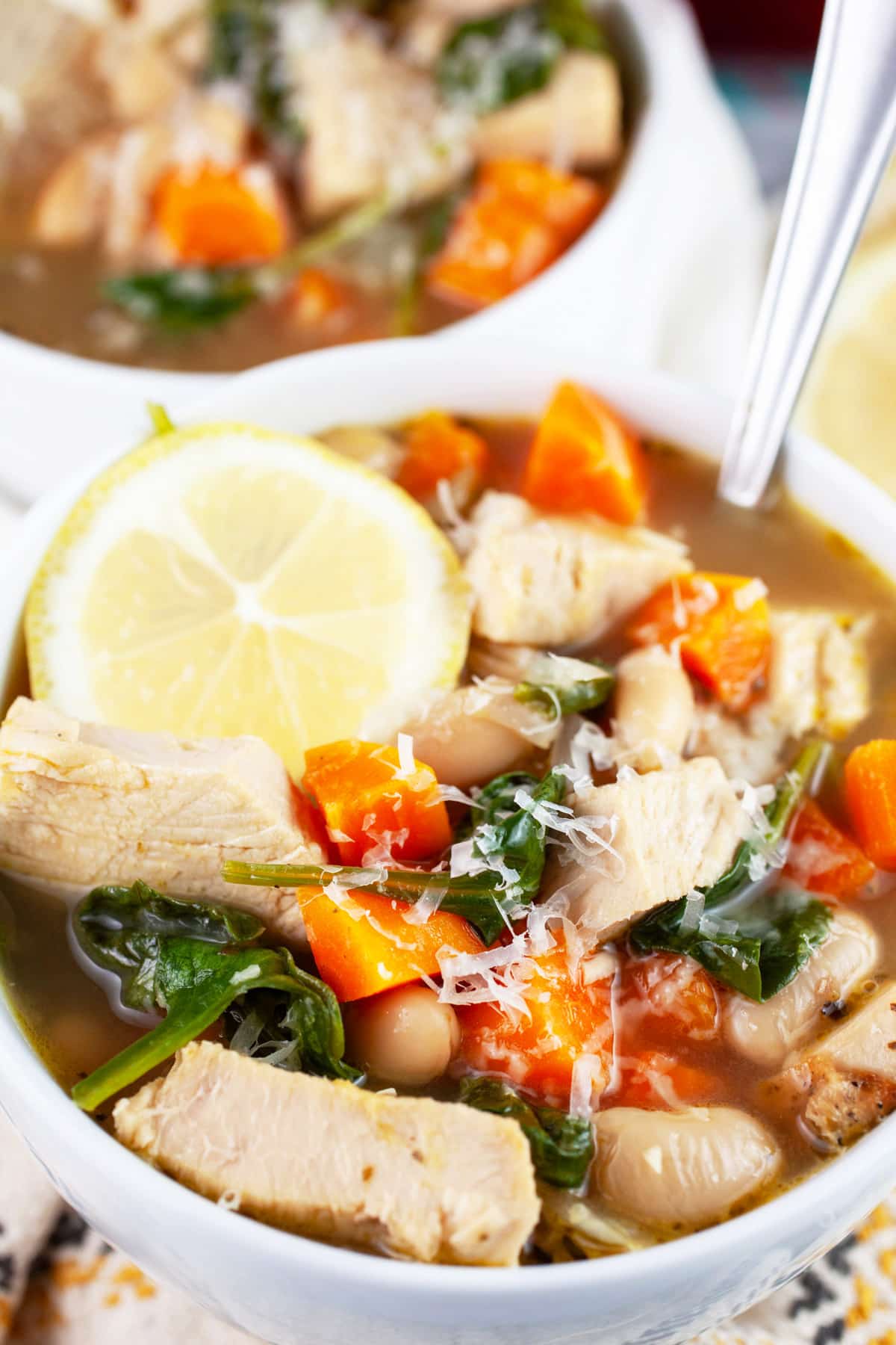 Turkey cannellini bean soup with Parmesan cheese and lemon wheel in white bowl with spoon.
