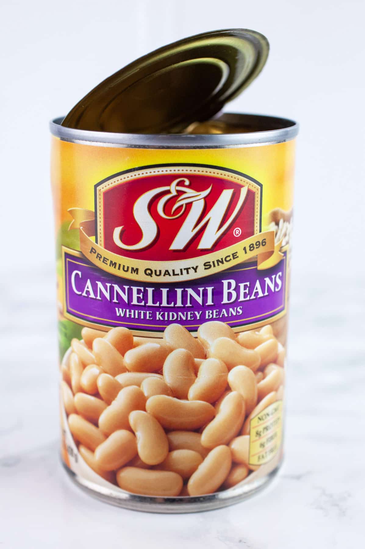 Opened can of cannellini beans on white surface.