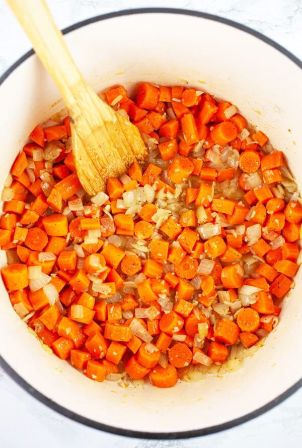 Minced garlic and onions and chopped carrots sauteed in Dutch oven with wooden spoon.