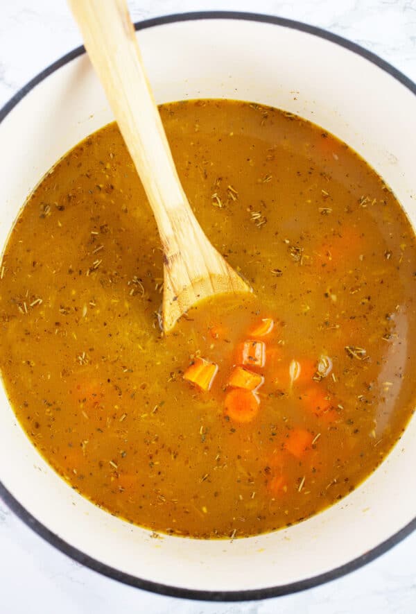 Uncooked turkey soup in Dutch oven with wooden spoon.