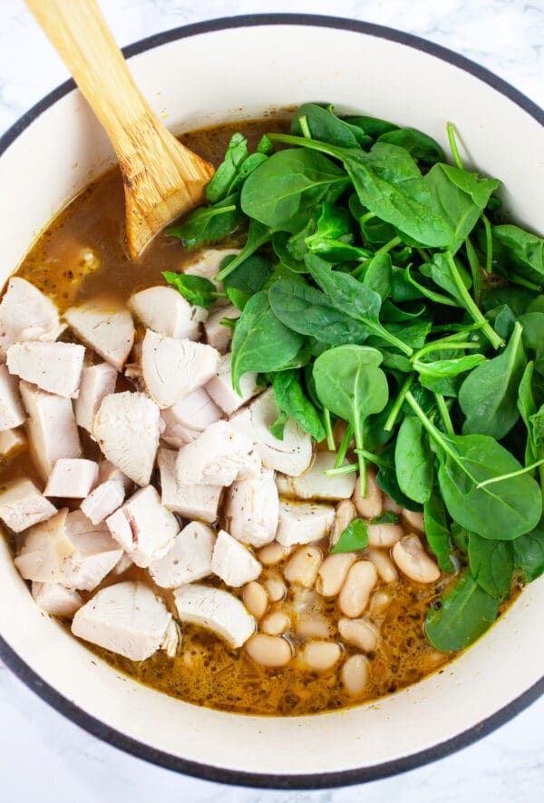 Diced, cooked turkey, white beans, and spinach in Dutch oven with wooden spoon.