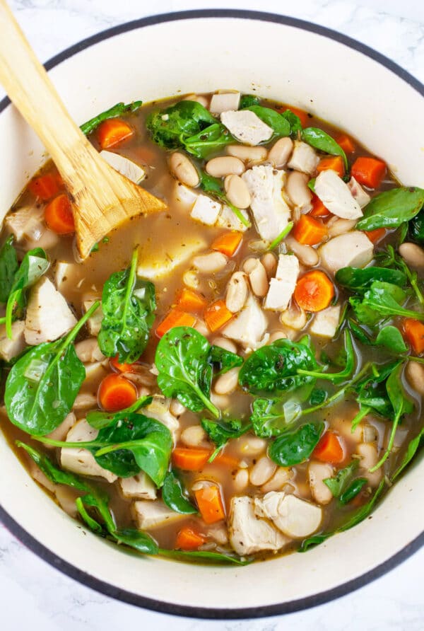 Turkey white bean soup with carrots and spinach in Dutch oven with wooden spoon.